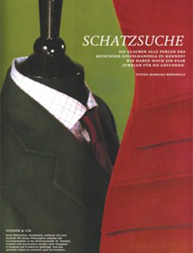 Eine dunkle Schaufensterpuppe trägt auf der linken Seite eine grüne Anzugsjacke, ein weißes Hemd und eine rote Krawatte. Auf der rechten Seite ist ein Teil eines roten Kleides zu sehen. Oben erscheint ein deutscher Text, darunter das Wort "SCHATZSUCHE".