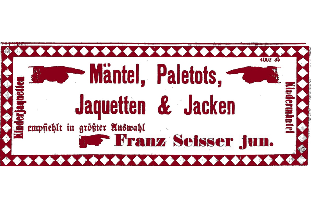 Ein altes deutsches Schild mit rotem Text lautet "Mäntel, Paletots, Jaquetten & Jacken" und "Franz Seisser jun.". Rote Hände zeigen nach links und rechts; dekorativer Rand mit Rauten und "Kinderjaquetten" und "Kinderarbeit" an den Seiten.