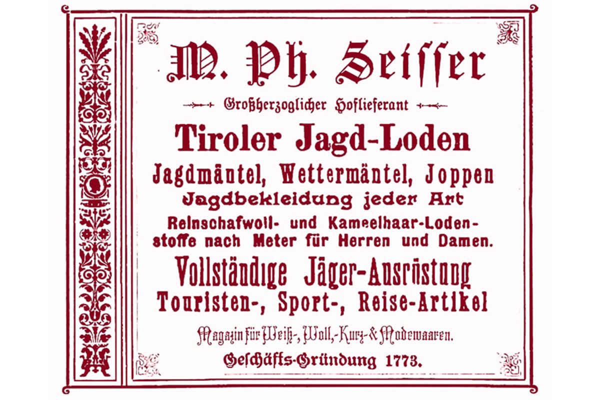Eine alte deutsche Anzeige mit roten Zierleisten und gotischer Schrift wirbt für M. Ph. Seissers Geschäft, das Tiroler Jagdbekleidung, Wettermäntel, Meterware und Reise- und Jagdausrüstung verkauft.